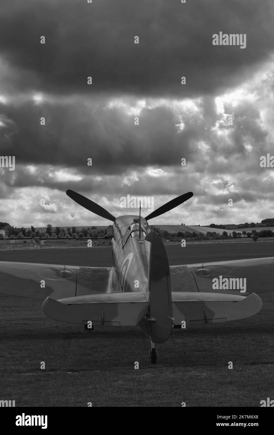 Schwarz-Weiß-Bild im Hochformat von einem spitfire geparkt auf Gras mit dunklen Wolken am Himmel, würde Buchcover passen Stockfoto