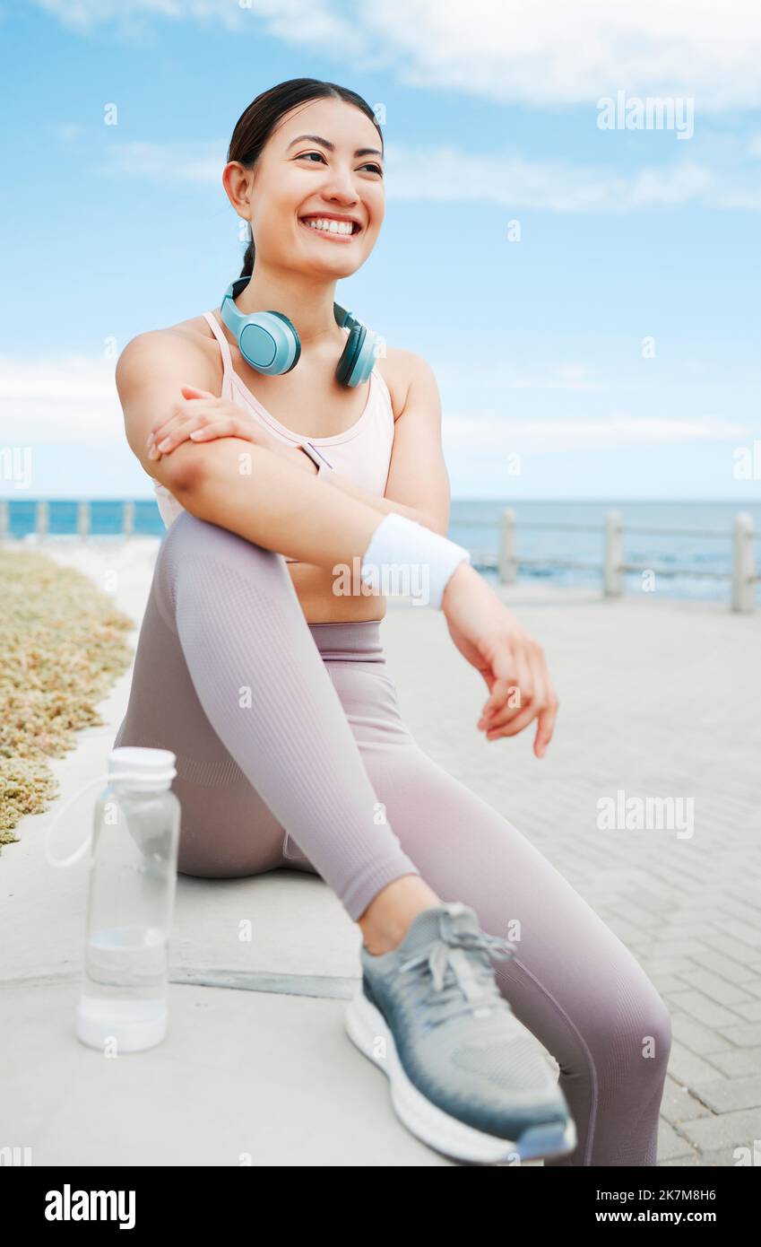 Fitness-Frau, glücklich und Strand-Bewegung während der Pause oder Ruhe beim Laufen auf der Promenade mit einer positiven Einstellung, Motivation und Ziel. Glücklich Stockfoto
