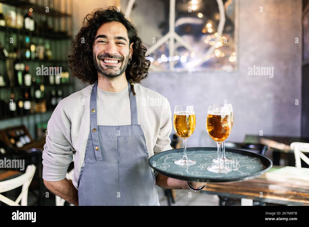 Freundliches Porträt eines selbstbewussten jungen Kellners, der ein Serviertablett mit Bier hält Stockfoto