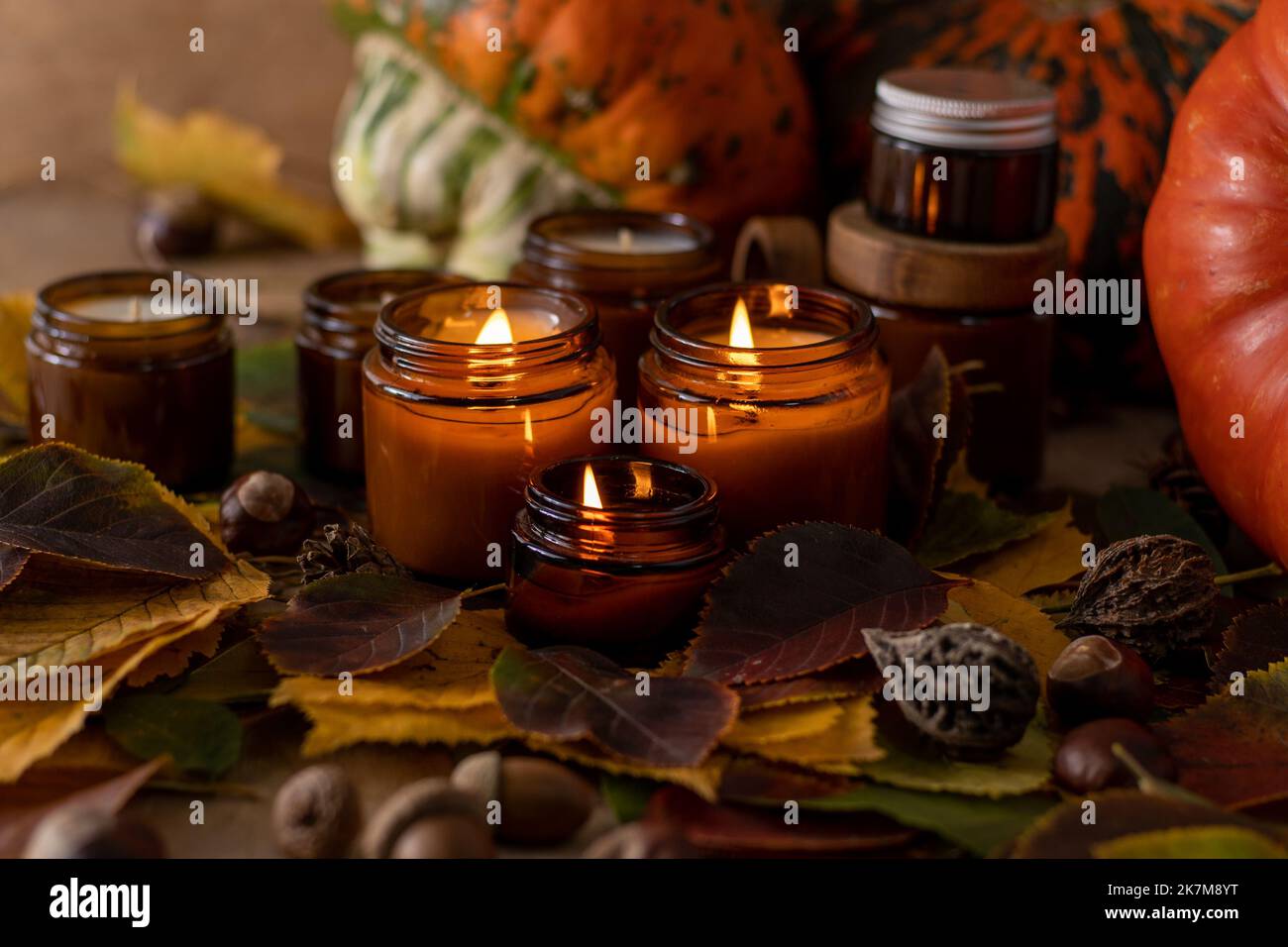Sojalkerzen brennen in Gläsern. Baumblätter, Kürbis. Komfort zu Hause. Kerze in einem braunen Glas. Duft und Licht. Handgemachte Duftkerze. Aromatherapie. Herbststimmung. Gemütliches Wohndekor im Herbst. Stockfoto