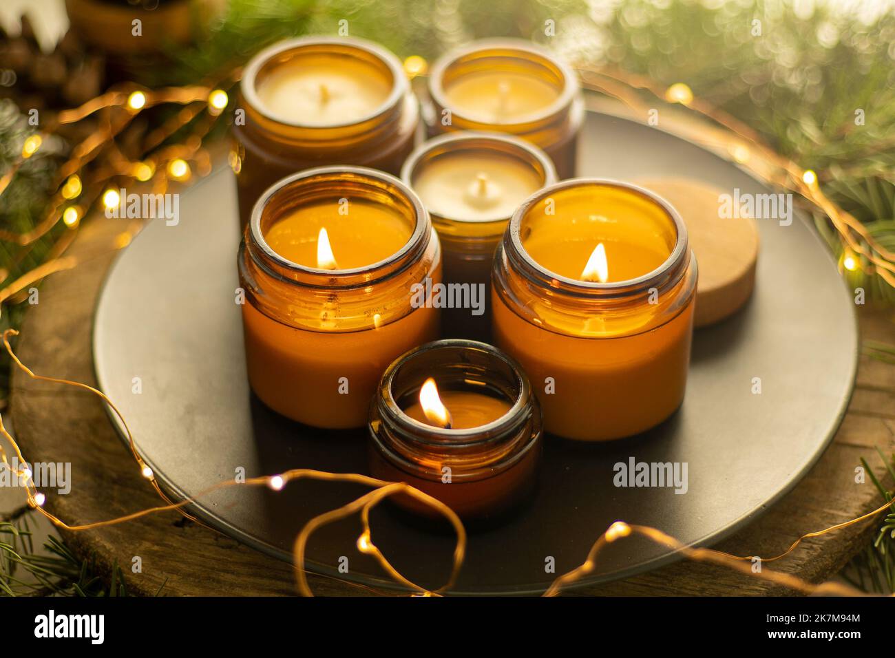 Sojalkerzen brennen in Gläsern. Komfort zu Hause. Kerze in einem braunen Glas. Duft und Licht. Handgemachte Duftkerze. Aromatherapie. Weihnachtsbaum und Winterstimmung. Gemütliche Einrichtung. Festliche Girlande-Dekoration Stockfoto