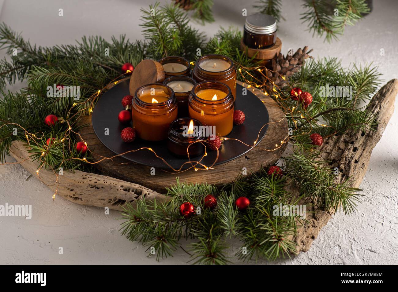 Sojalkerzen brennen in Gläsern. Komfort zu Hause. Kerze in einem braunen Glas. Duft und Licht. Handgemachte Duftkerze. Aromatherapie. Weihnachtsbaum und Winterstimmung. Gemütliche Einrichtung. Festliche Girlande-Dekoration Stockfoto