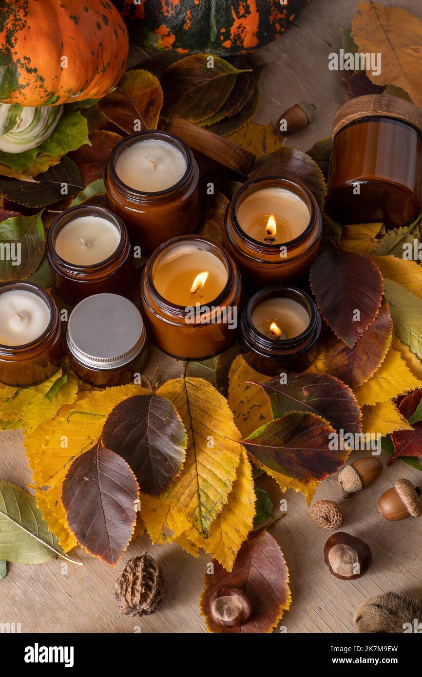 Sojalkerzen brennen in Gläsern. Baumblätter. Komfort zu Hause. Kerze in einem braunen Glas. Duft und Licht. Handgemachte Duftkerze. Aromatherapie. Herbststimmung. Gemütliches Wohndekor im Herbst. Festliche Dekoration. Stockfoto