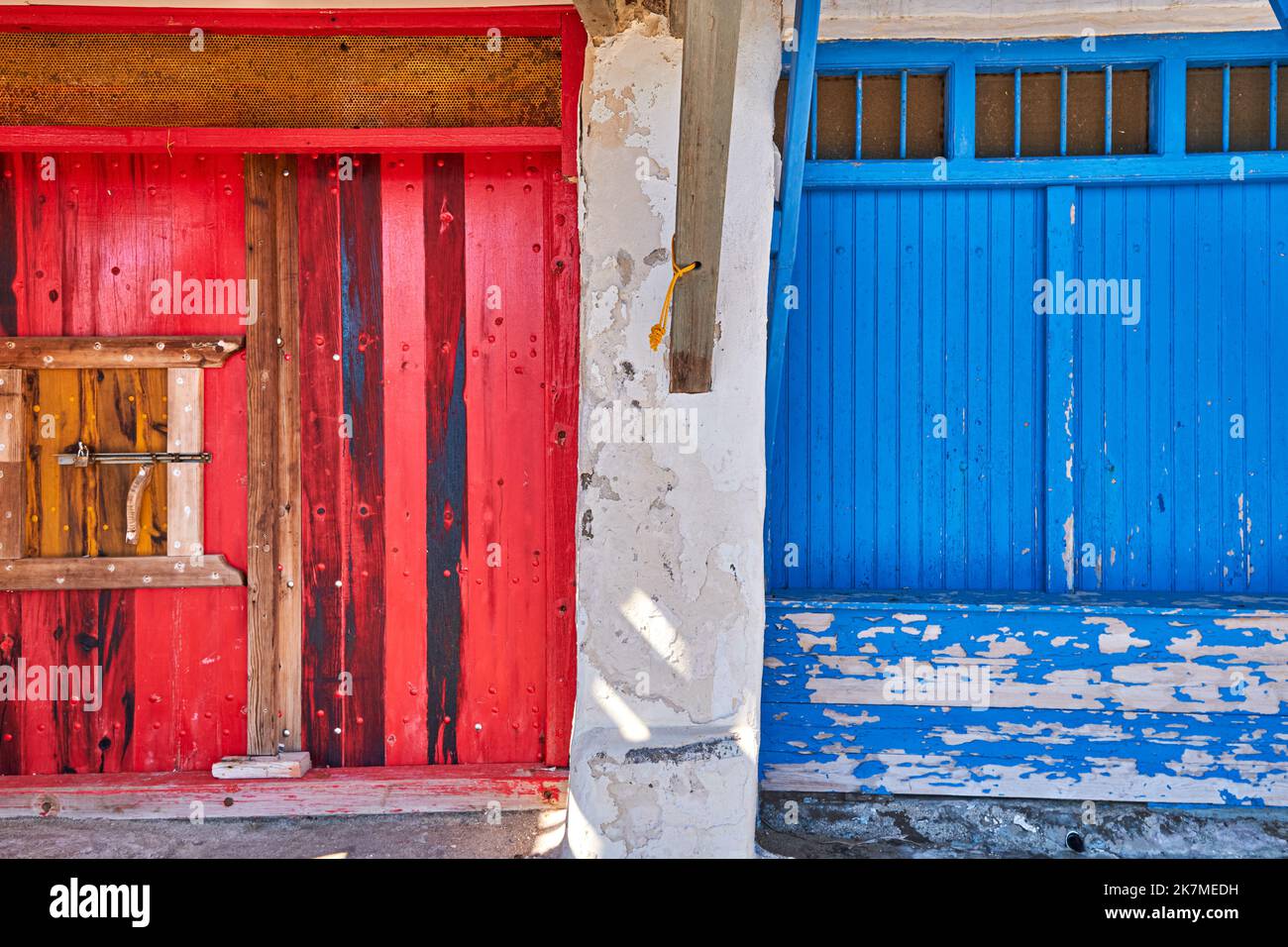 Farbenfrohe blaue, rote Garagentore für Boote, Klima Fischerdorf, Griechenland. Bemalte und verwitterte Holztüren, weiß getünchte Wände. Stockfoto