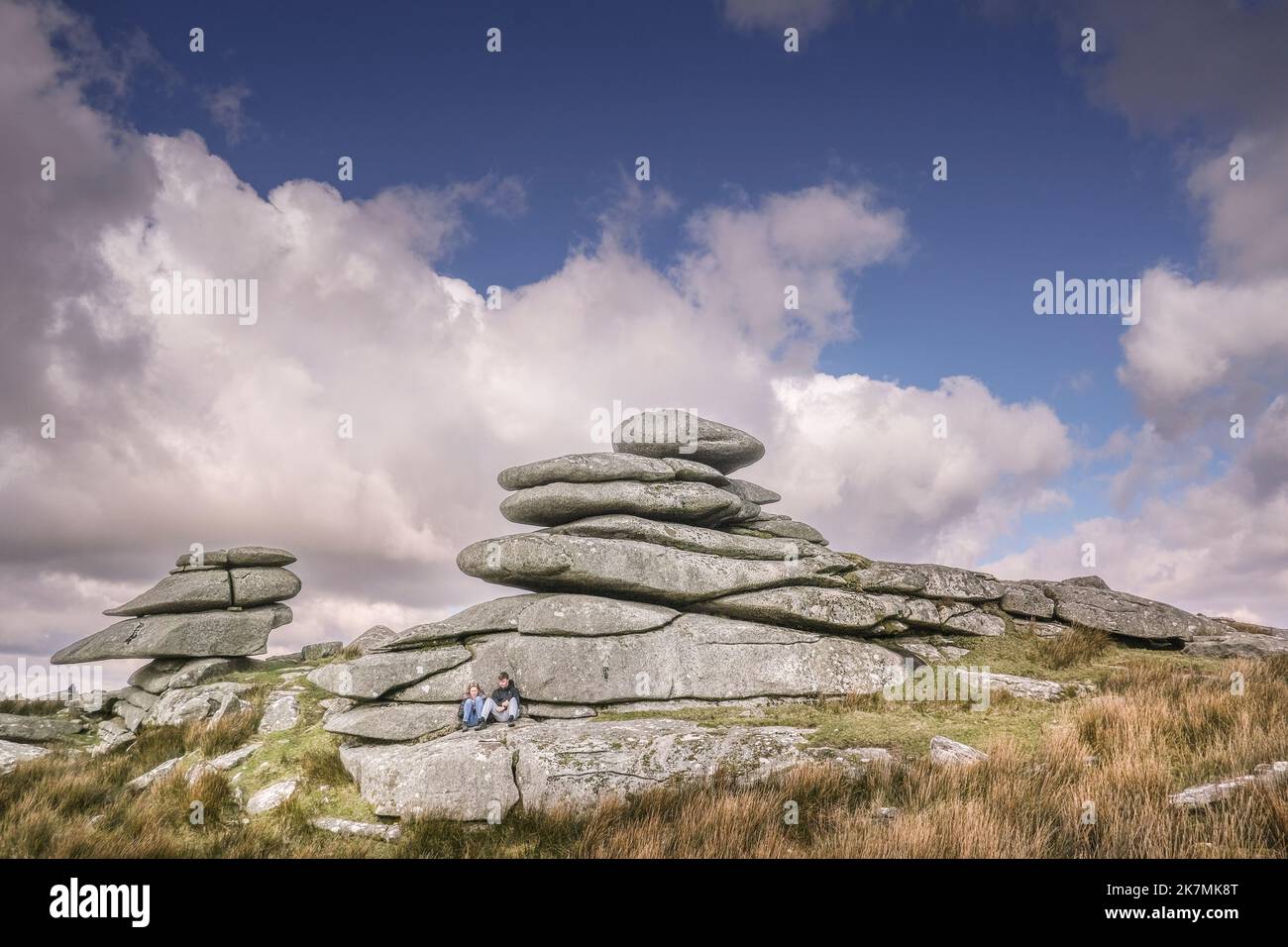 Ein junges Paar, das sich unter einem hoch aufragenden Granitfelsen-Stapel auf dem Stowes Hill auf Bodmin Moor in Cornwall entspannt. Stockfoto