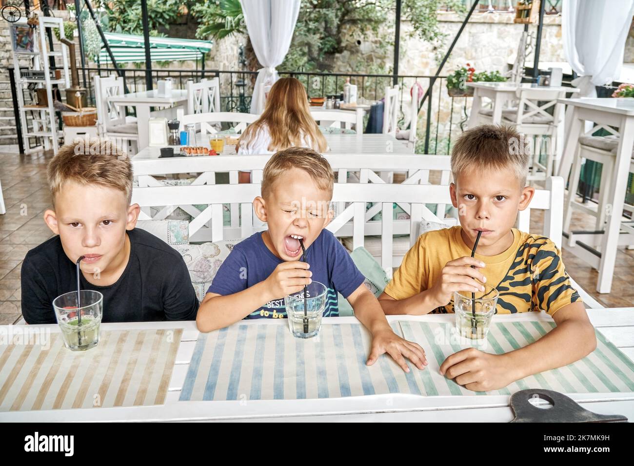 Brüder sitzen am Holztisch im Restaurant und trinken Limonade aus Gläsern mit Trinkhalmen. Geschwister genießen es, gemeinsam ins Restaurant zu gehen, um Mahlzeiten zu probieren Stockfoto