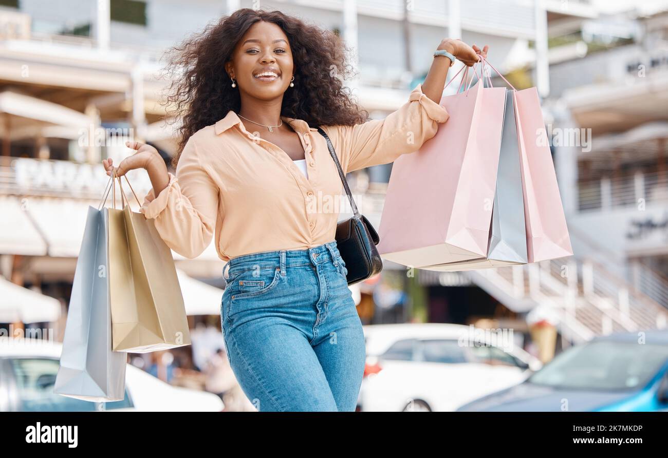 Shopping, Mode und Einzelhandel, eine schwarze Frau mit Lächeln und Designer-Boutique-Einkaufstaschen vor einem Einkaufszentrum. Zufriedener Kunde oder Einflussnehmer nach Rabatt Stockfoto