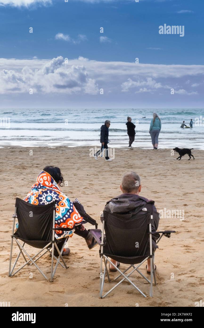 Zwei Urlauber sitzen auf Klappstühlen am Fistral Beach und blicken auf das Meer in Newquay in Cornwall in England. Stockfoto