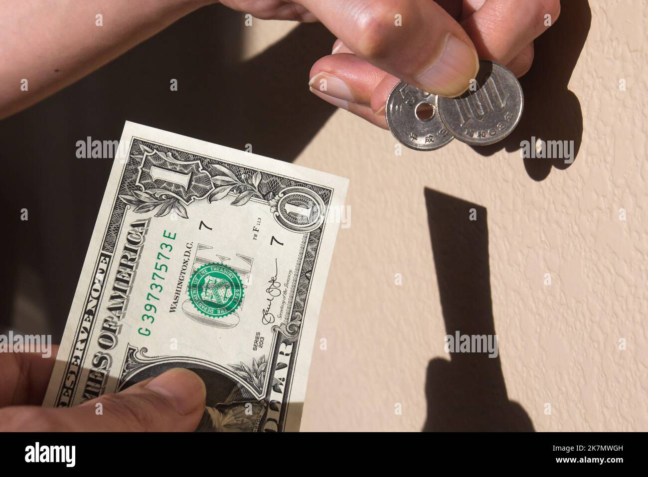 Ein asiatischer Mann übergibt einen US-Dollar-Schein im Austausch für 150 JPY, der aktuelle ungefähre Kurs im Oktober 2022. Ihr Schatten reflektiert auf dem w Stockfoto