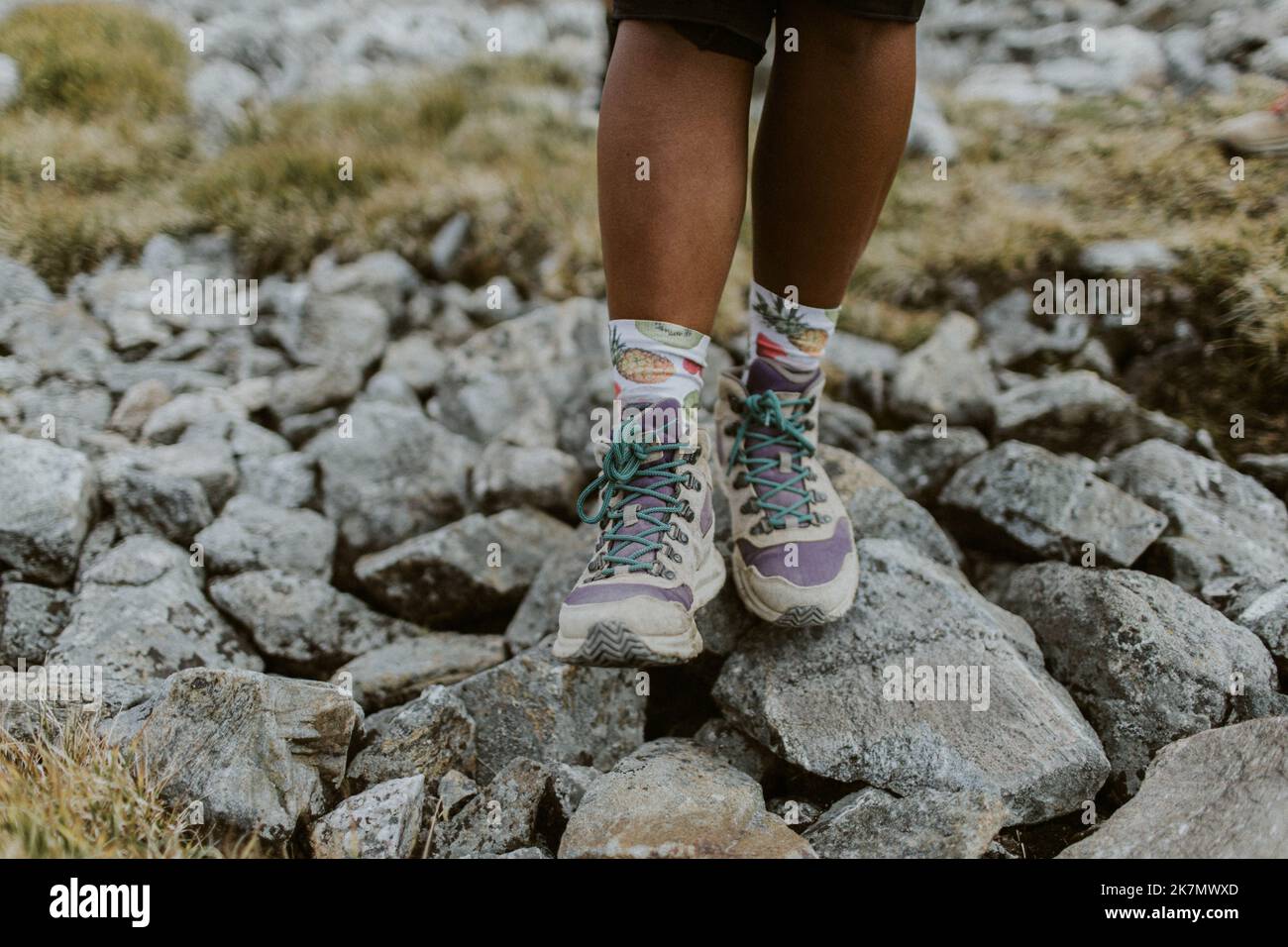 Eine Nahaufnahme von Wanderschuhen mit violetten Details, türkisfarbenen Schnürsenkeln und Socken mit Fruchtmuster Stockfoto