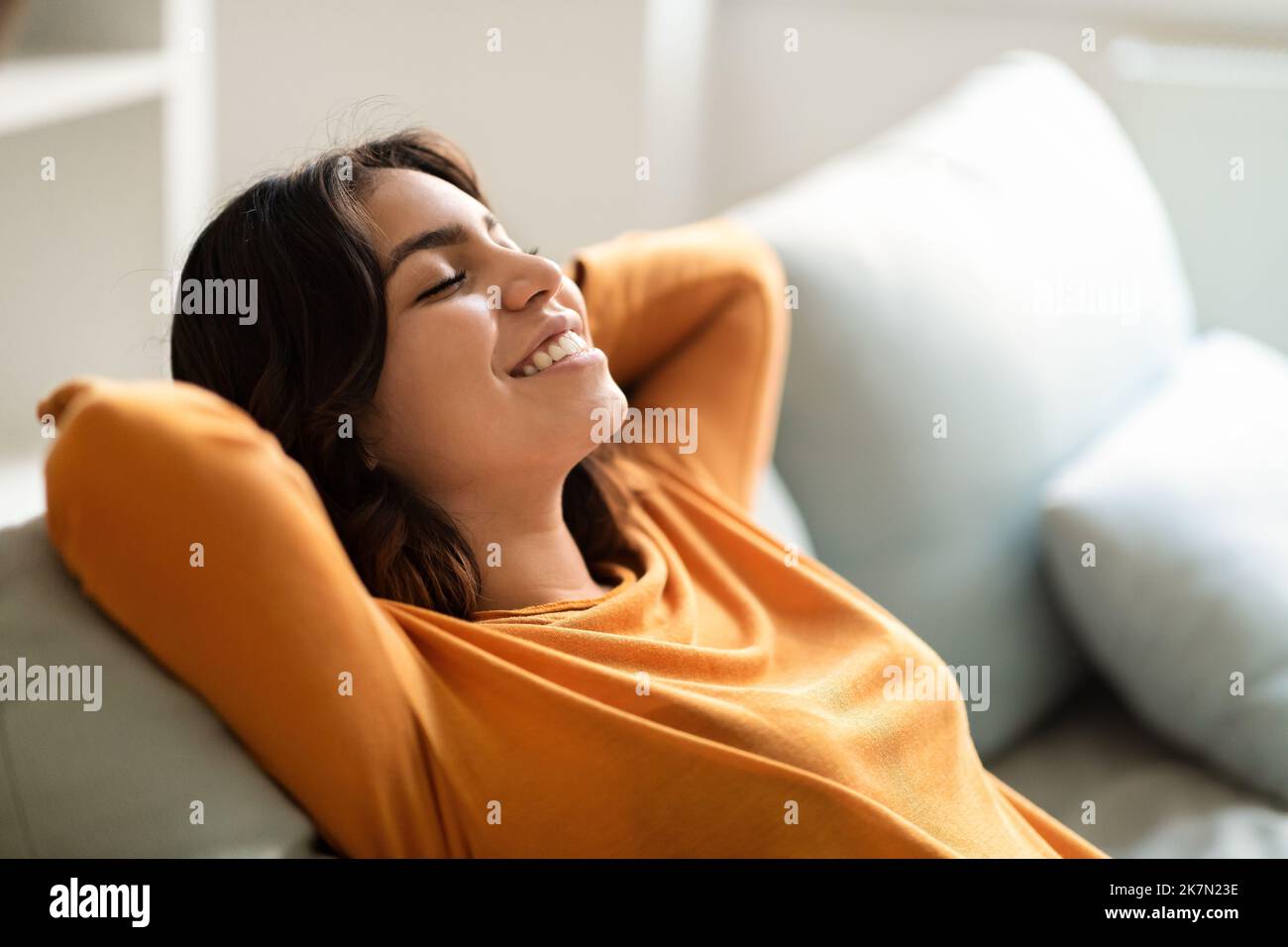 Komfort Zu Hause. Porträt Einer Lächelnden Jungen Arabischen Frau, Die Sich Auf Der Couch Zurückschief Stockfoto