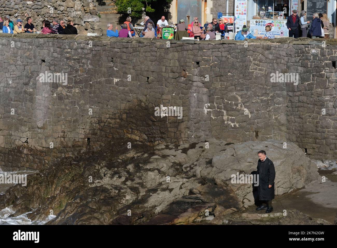 Ein einsamer Mann, der auf einigen Felsen steht, während sich die Menschen darüber Vergnügen. Stockfoto