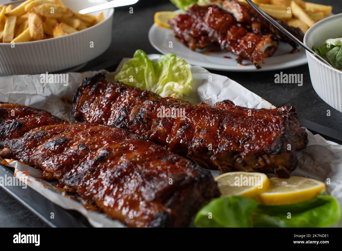 Gegrilltes Schweinefleischgericht mit frisch gegrillten Spareribs, hausgemachten pommes frites und Salat auf einem Esstisch Stockfoto