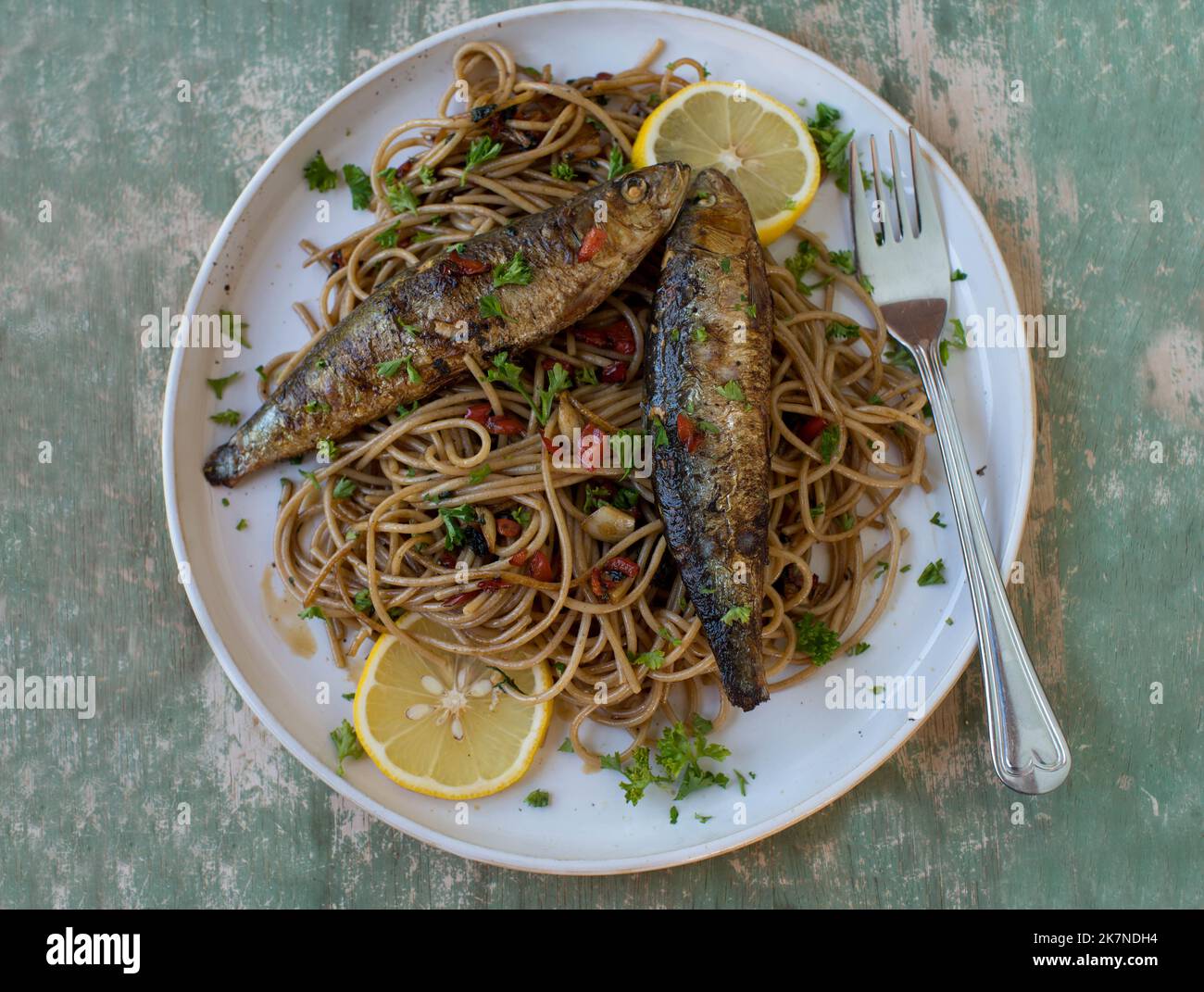 Gebratene Sardinen mit Vollkornpasta, gekocht mit Olivenöl, Knoblauch, Paprika und Petersilie auf einem Teller Stockfoto