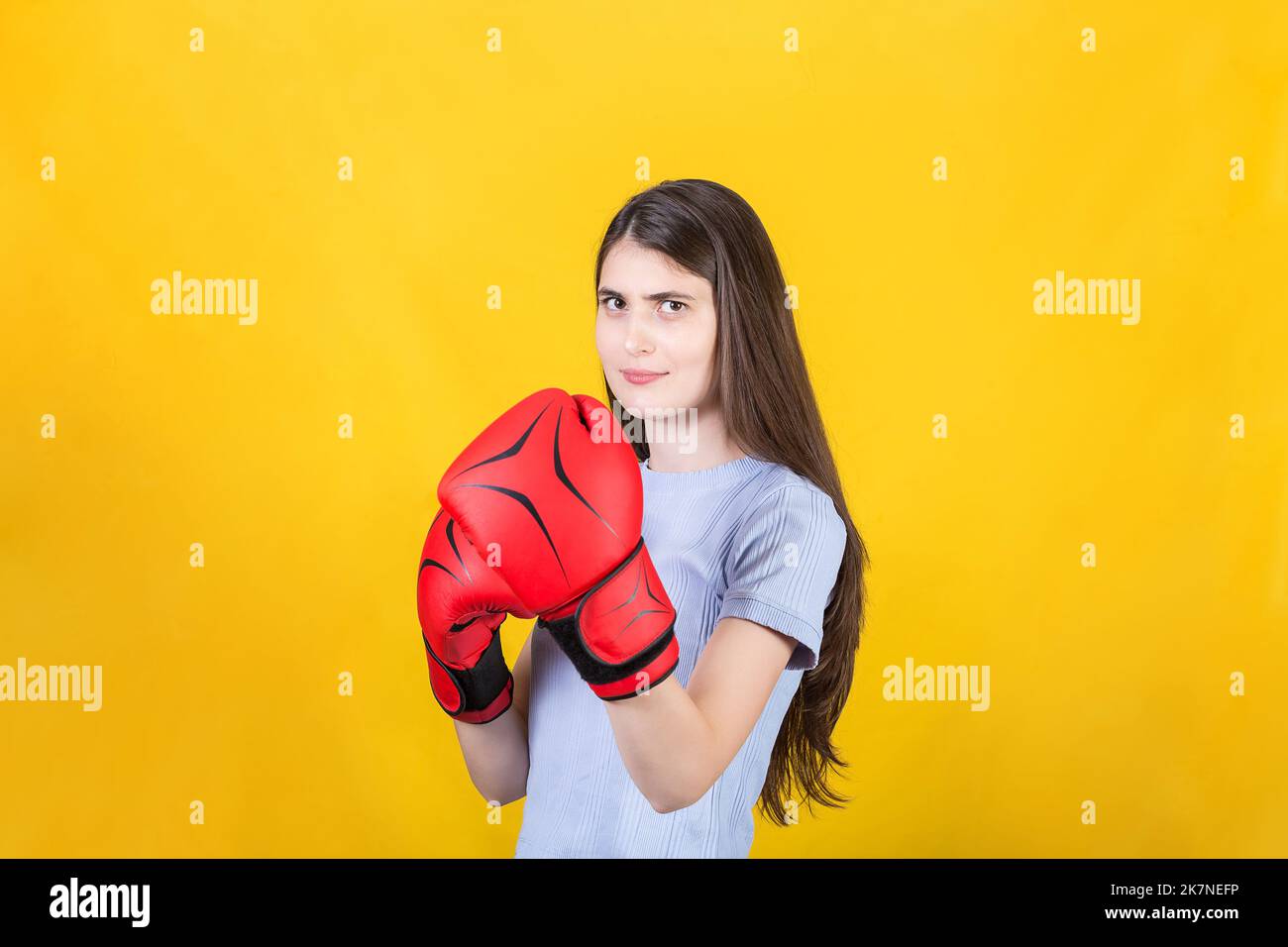 Selbstbewusste junge Frau mit roten Boxhandschuhen steht in Kampfposition. Portrait eines starken und entschlossenen Mädchens, das auf Yello isoliert auf den Kampf vorbereitet ist Stockfoto