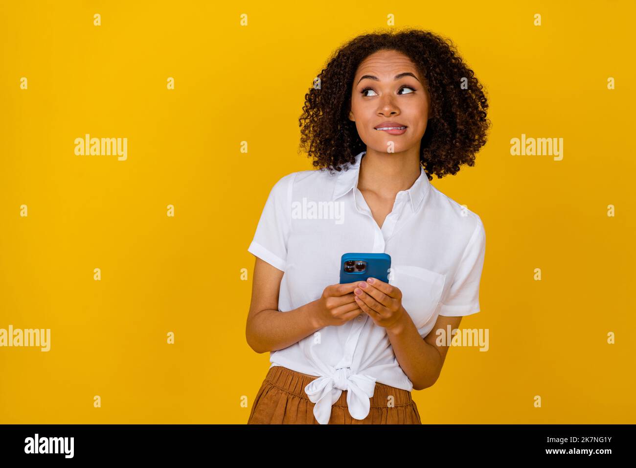 Portrait von ziemlich gesinnten Dame halten Telefon beißen Lippen suchen leeren Raum hmm tief isoliert auf gelben Hintergrund Stockfoto