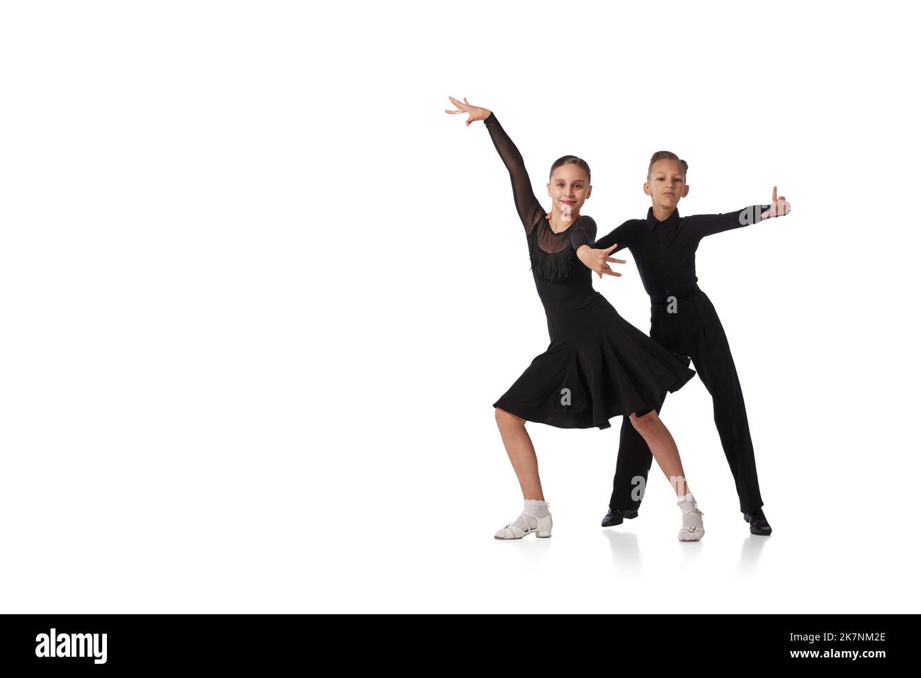 Tanzpaar. Zwei Kinder, Mädchen und Jungen im Schulalter in schwarzen Bühnenkostümen, tanzen auf weißem Hintergrund isoliert den Tanzsaal. Bewegung, Action, Hobbys Stockfoto