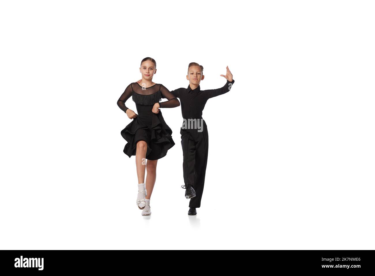 Tanzpaar. Zwei Kinder, Mädchen und Jungen im Schulalter in schwarzen Bühnenkostümen, tanzen auf weißem Hintergrund isoliert den Tanzsaal. Bewegung, Action, Hobbys Stockfoto