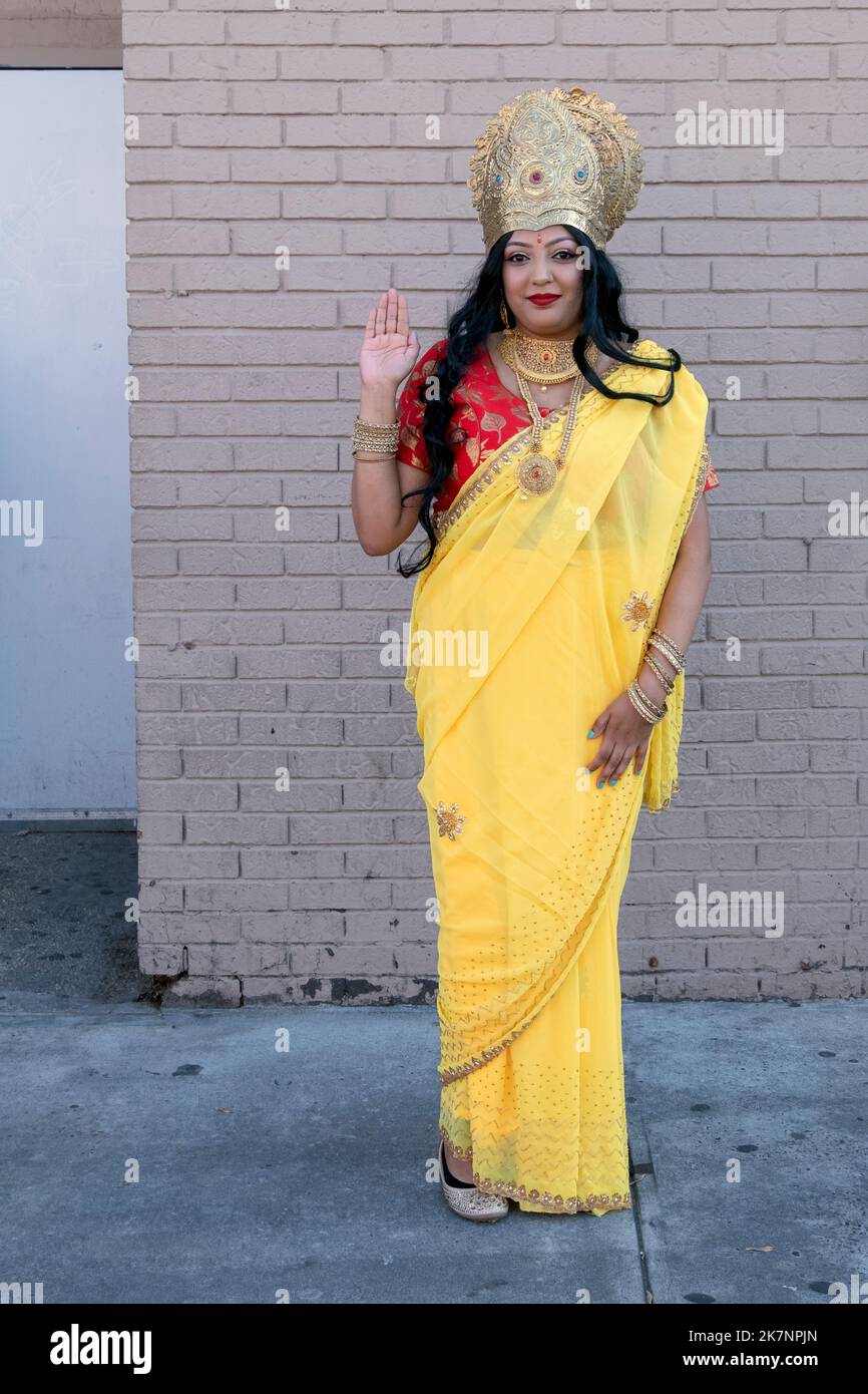 Eine hübsche Hindu-Frau, die einen gelben Sari und eine Krone trägt und als Göttin Lakshmi gekleidet ist. Auf der Diwali 2022 in Queens, New York City. Stockfoto
