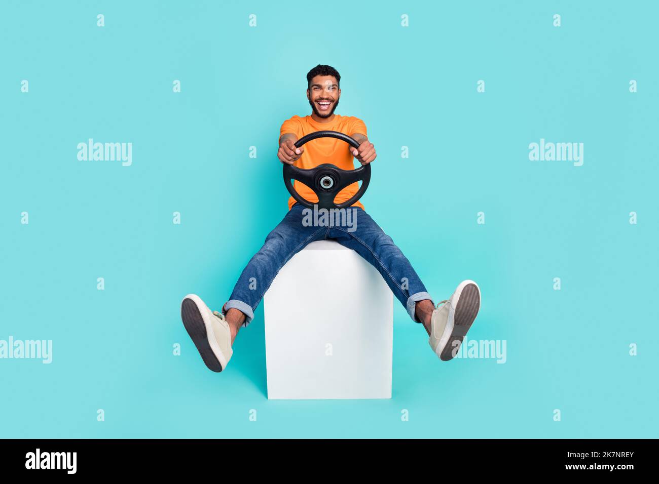 In voller Länge Foto von aufgeregt fröhliche Person sitzen Podium Hände halten Rad isoliert auf cyanfarbenem Hintergrund Stockfoto