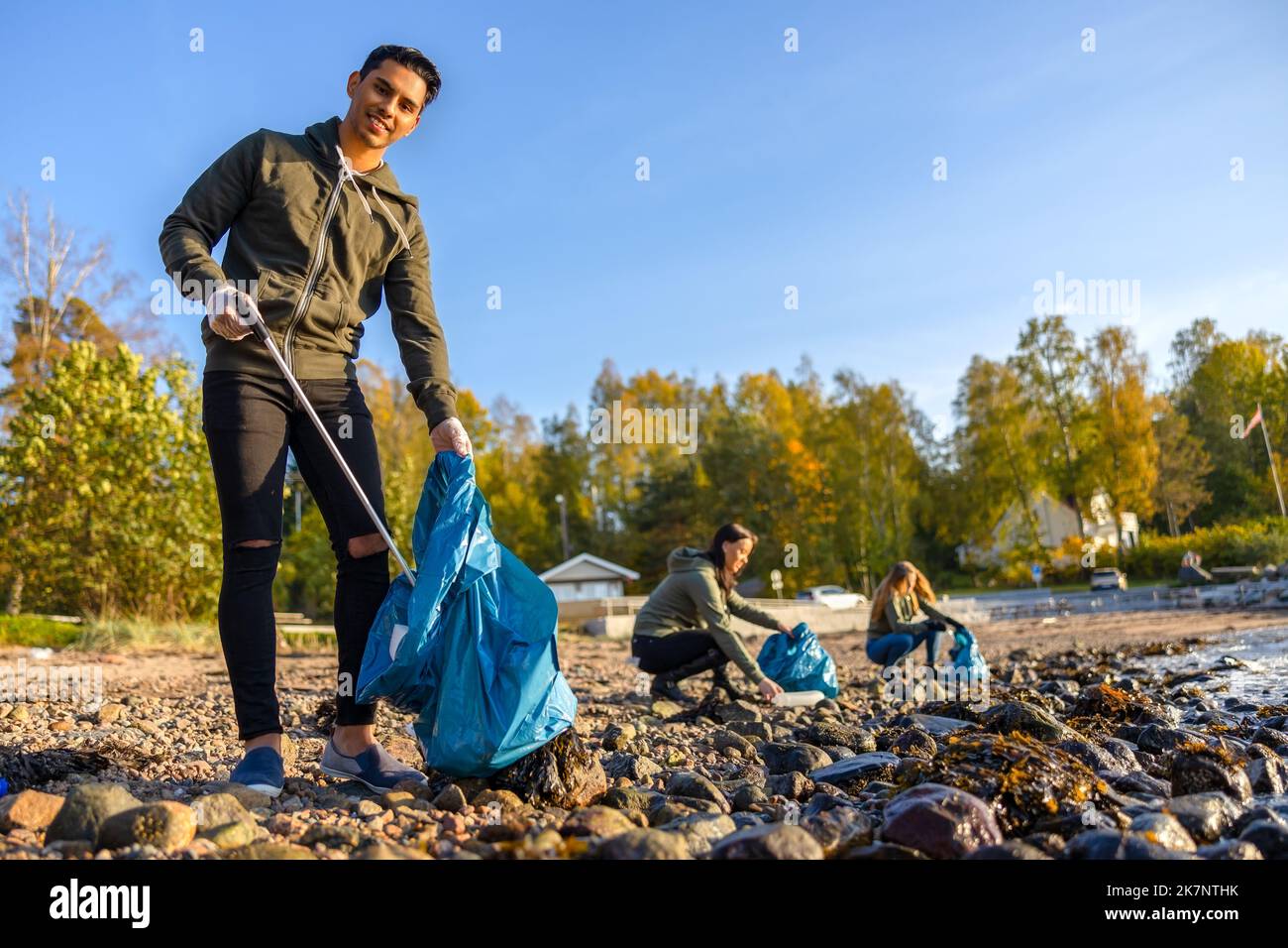 Mann, der am sonnigen Tag mit einer Gruppe von Freiwilligen den Strand putzt Stockfoto