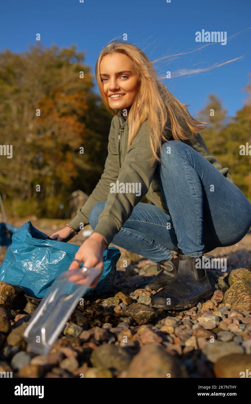 Lächelnde junge Frau im Team zum Umweltschutz, die am Strand Plastik abholt Stockfoto