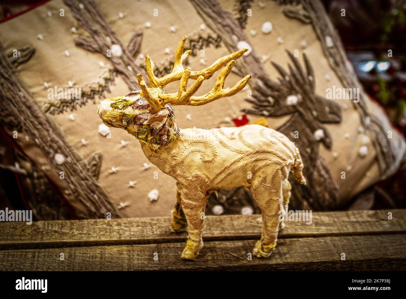 Gestickter gestopfter Elch, der auf rauem Holz steht, mit Elchen im verschneiten Waldkissen im Hintergrund Stockfoto