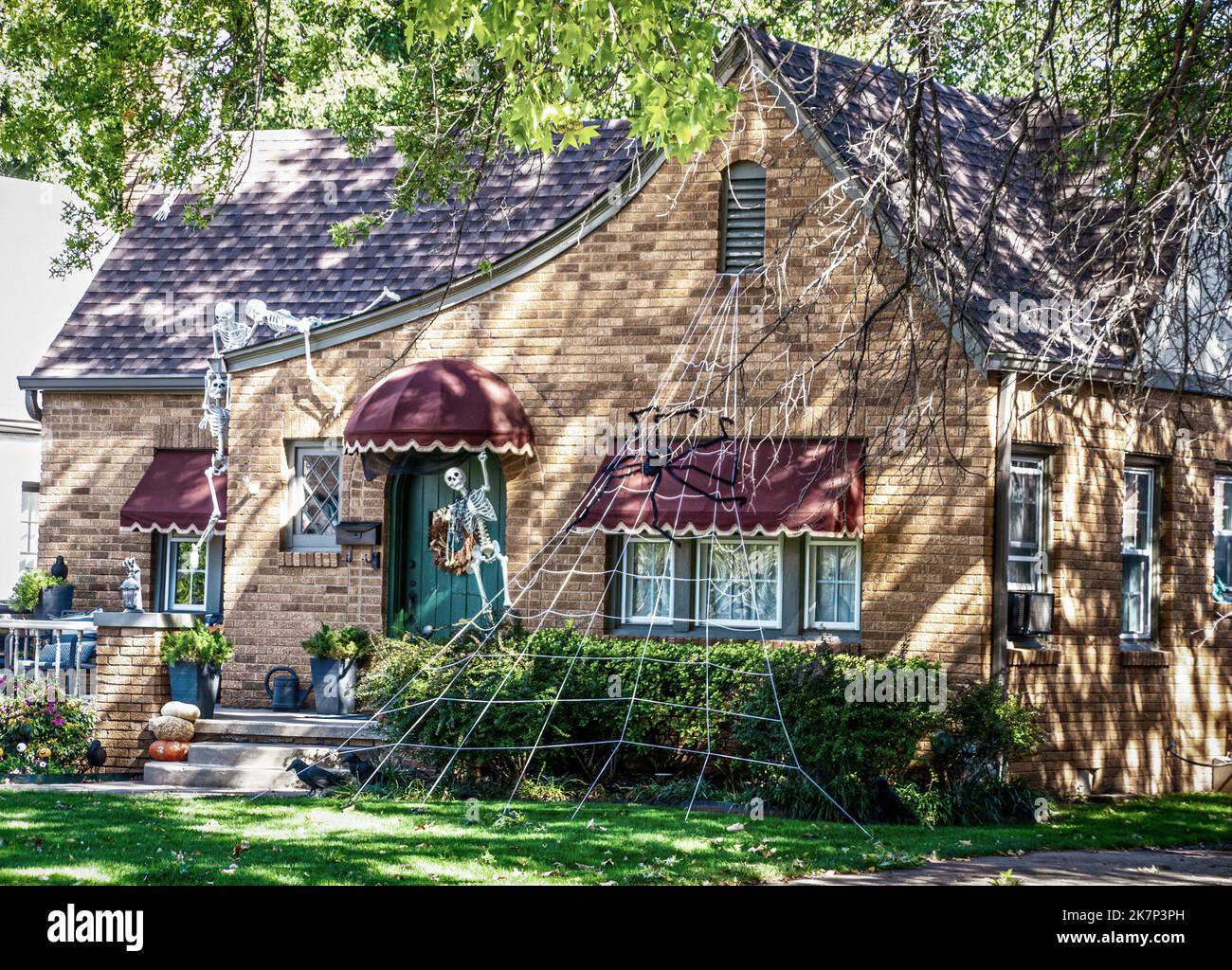 Gruseliges Vintage Cottage mit Markisen ist für Halloween mit Skeletten geschmückt, die auf dem Dach krabbeln und einem riesigen Spinnennetz Stockfoto