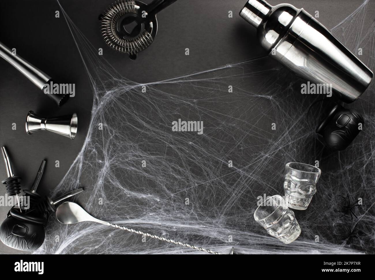 Verschiedene Bar-Accessoires wie: Ein Schüttler, Schlammler, Sieb, sowie ein Bar-Löffel und ein Messstapel liegen vor der Kulisse eines Spinnennetzes auf Stockfoto