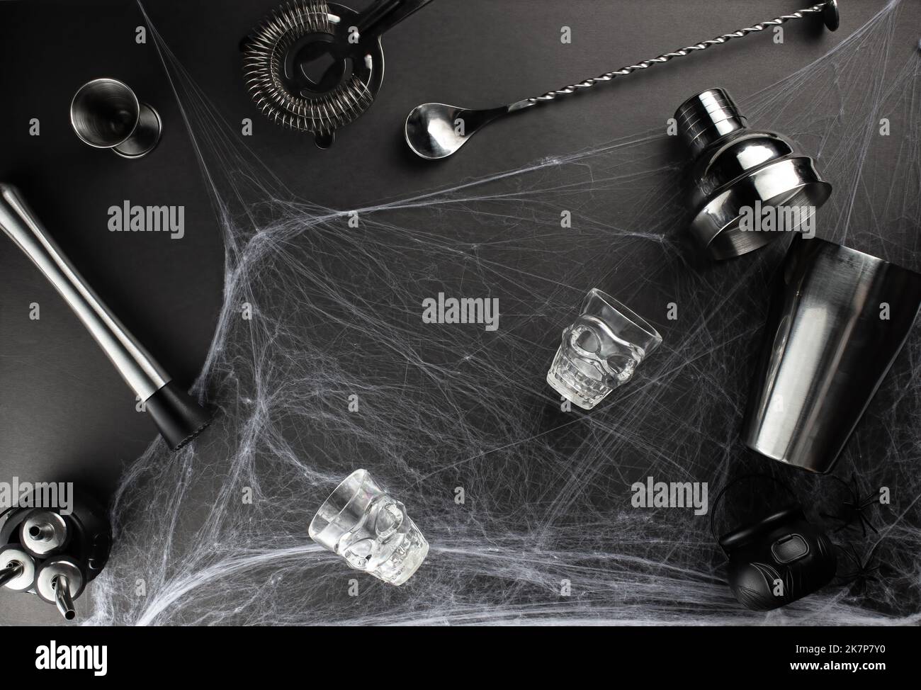 Verschiedene Bar-Accessoires wie: Ein Schüttler, Schlammler, Sieb, sowie ein Bar-Löffel und ein Messstapel liegen vor der Kulisse eines Spinnennetzes auf Stockfoto