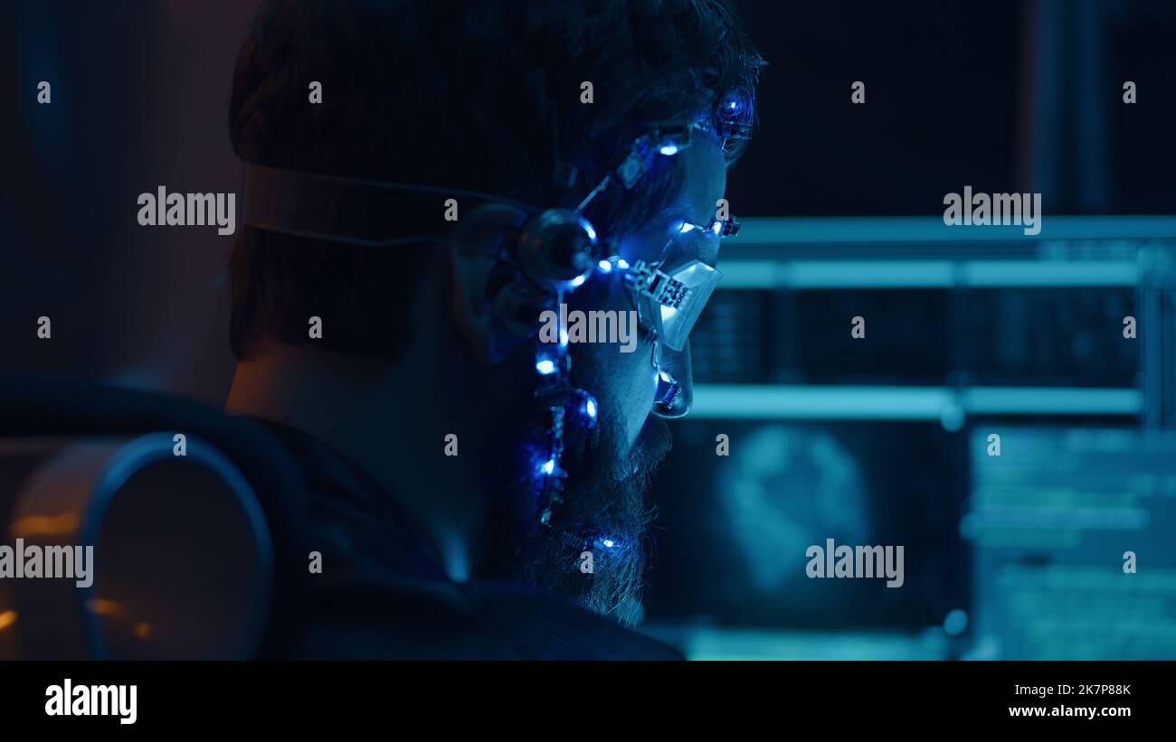 Rückansicht eines Brünetten Typen, der ein futuristisches Headset mit LED-Leuchten trägt, die Programme anschließt und Code mithilfe eines mehrfachen Computerbildschirms entwickelt. Cypperpunk-Stil. Sci-Fi-Hintergrund. Neonlichter. Stockfoto