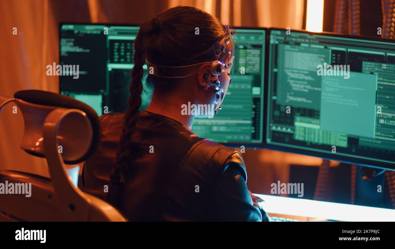 Rückansicht eines Cyberpunk-Mädchens auf der Tastatur. Mehrere Computer-Bildschirm mit Zeichenketten von Codes vor ihr. Entwicklungscodes für futuristische Software. Neonlichter im Hintergrund. Stockfoto