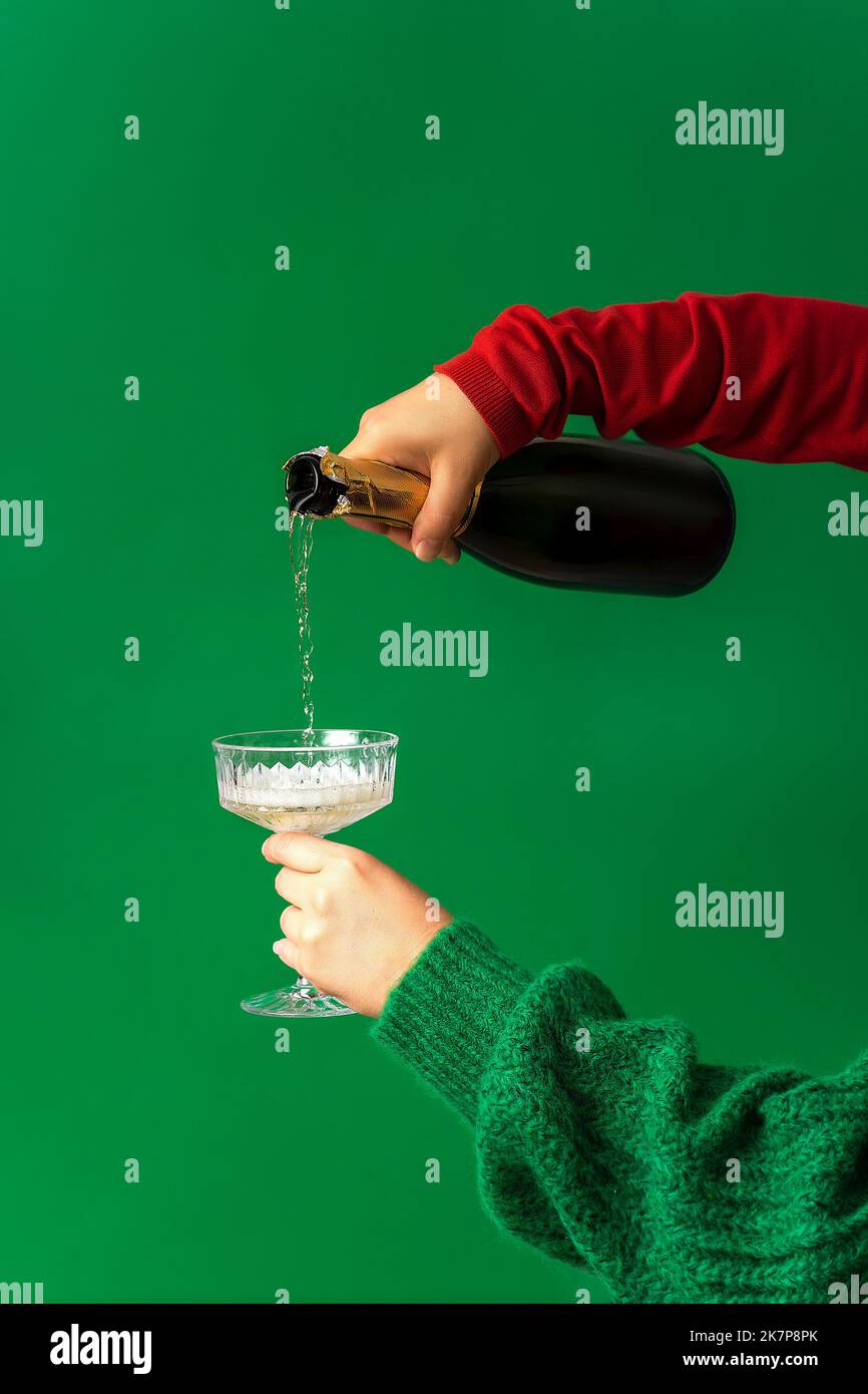 Festliches Hintergrundkonzept für Weihnachtsfeier, handgeschüttete Champagner, Wein in ein Glas Minimalismus, grüner Hintergrund, Weihnachten und Silvester-Party c Stockfoto