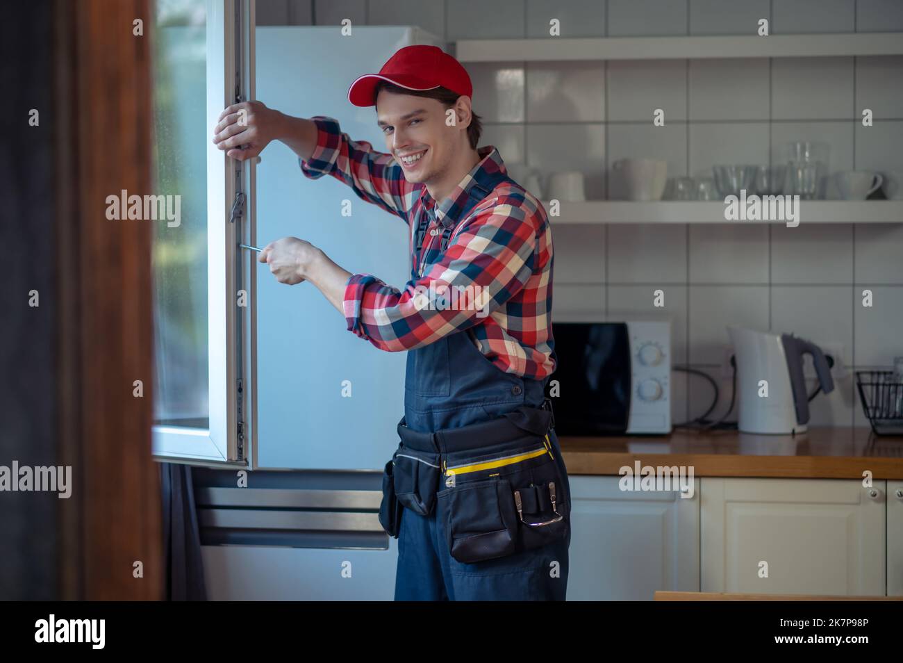 Zufrieden junger Reparaturmann, der das Fenster in einer Kundenküche installiert hat Stockfoto