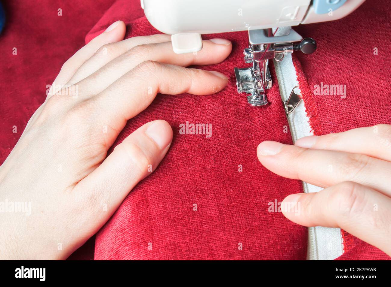 Schneiderhände nähen den Reißverschluss an roten Kleidungsstücken von einer modernen Nähmaschine mit speziellem Nähfuß. Nähprozess Stockfoto