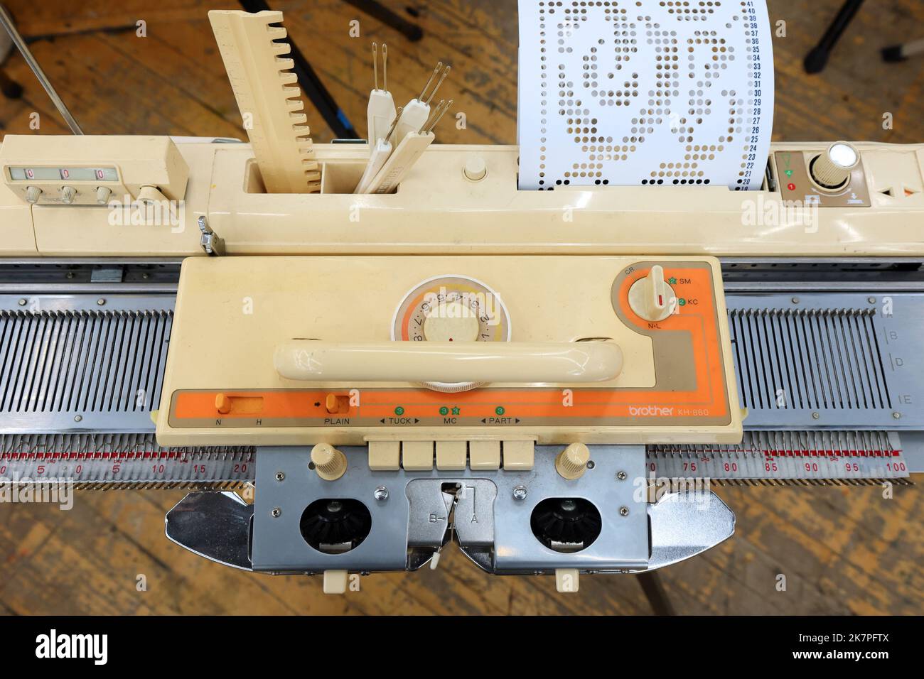 Eine Brother KH860 Strickmaschine mit Reihenzähler, Lochkarte, Kutsche und angebrachten Platinen auf einem Bett aus Stricknadeln. Stockfoto