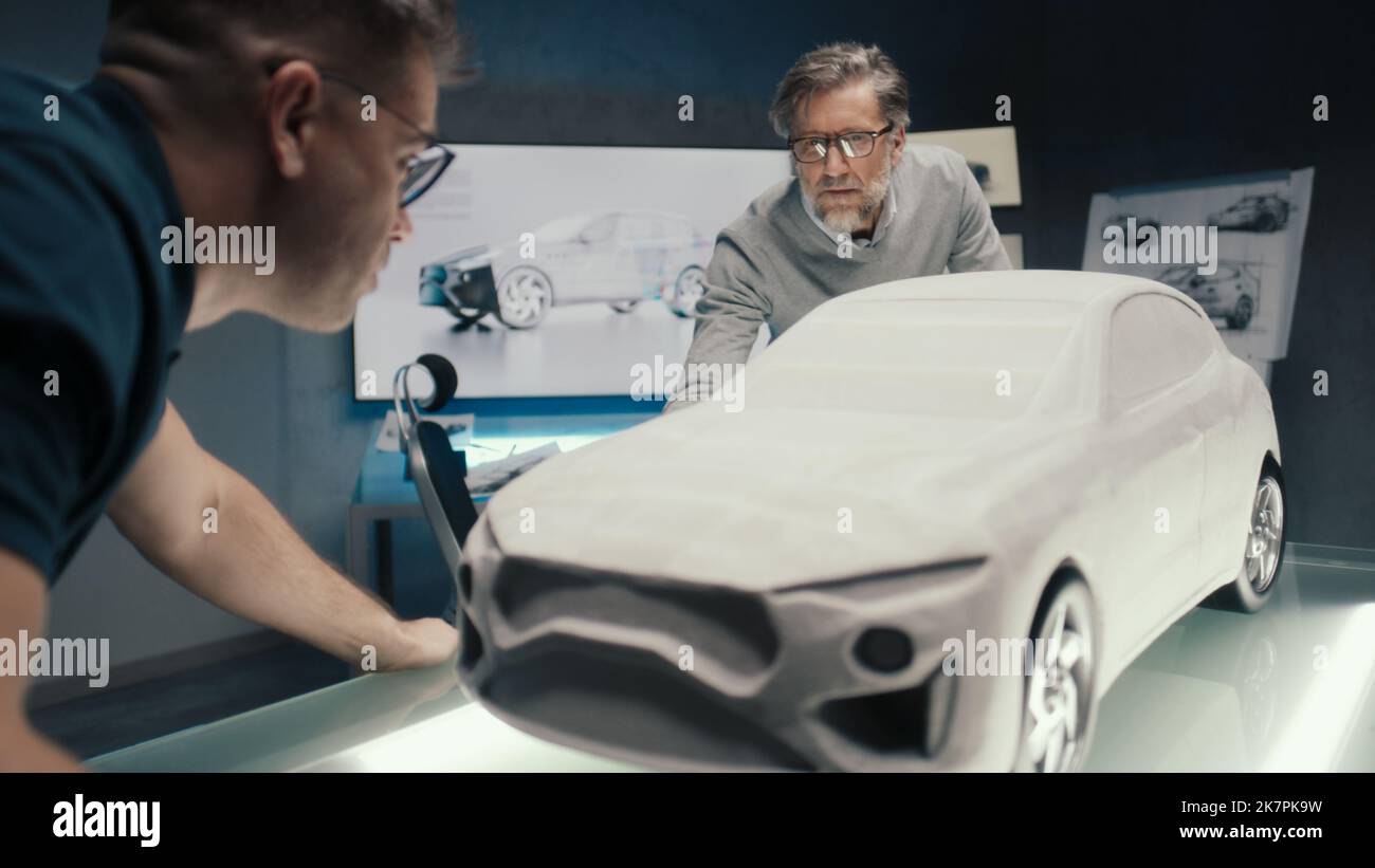 Automobilingenieure arbeiten in einem Autodesignstudio mit einer an der Wand montierten LED. Diskutieren Sie die Gestaltung der Skulptur des Prototyps Auto Modell auf einem Glastisch platziert. Stockfoto