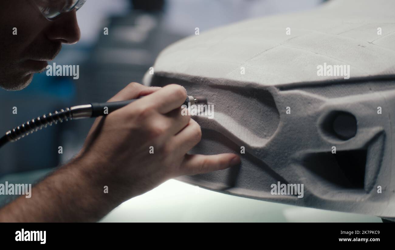 Der leitende Autodesigner und -Entwickler verwendet ein Drehwerkzeug in Stiftform, um die Rake-Skulptur eines Prototyps eines Automodells in einem Hightech-Studio zu honen. Führt die Konstruktionskorrekturen durch. Automobilindustrie. Stockfoto