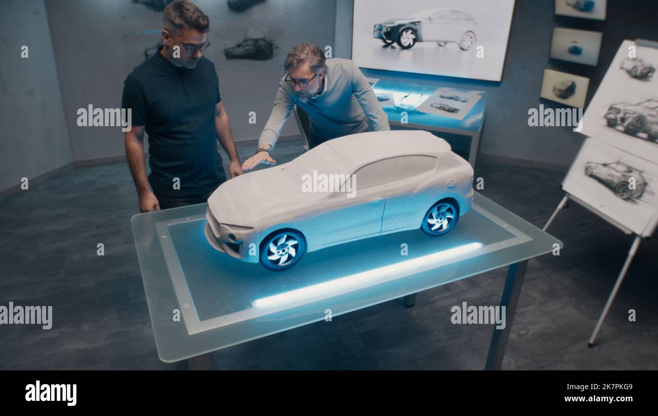 Leitende Automobilentwickler nehmen die Designkorrekturen vor, indem sie die Skulptur des Prototyps auf einem Glastisch betrachten. High-Tech-Büro mit LED und Auto Skizzen. Stockfoto