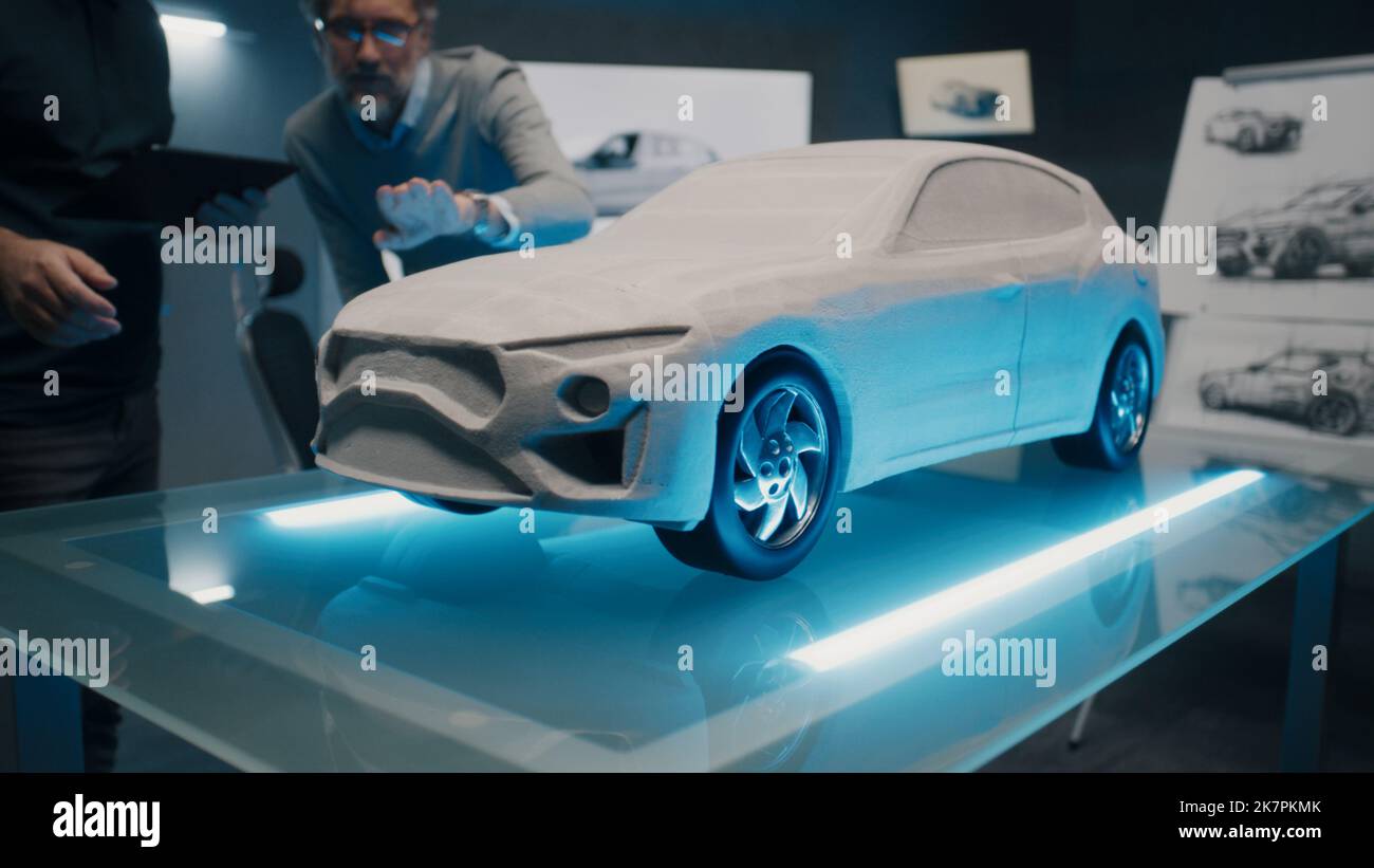 Erfahrene Automobil-Designer und Auto-Entwickler diskutieren das Design vor einem Rake-sculpt-Prototyp-Automodell. Ingenieure verwenden ein digitales Touchscreen-Tablet in einem High-Tech-Labor. Stockfoto
