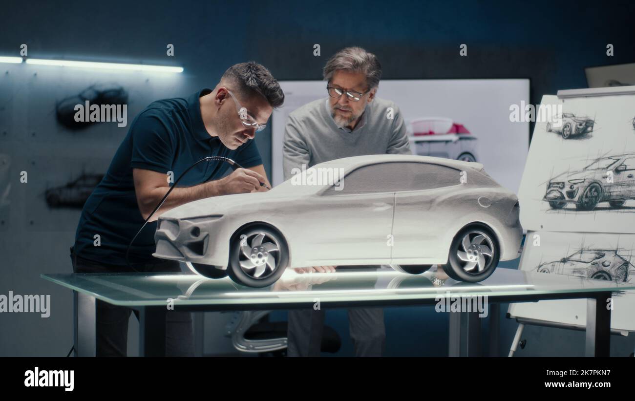 Zwei erfahrene Automobilingenieure diskutieren das Fahrzeugdesign anhand der Skizzen auf dem Brett. Korrekturen an der Prototyp-Rechen-Skulptur mit einem rotierenden Werkzeug mit drehender Spitze. Stockfoto