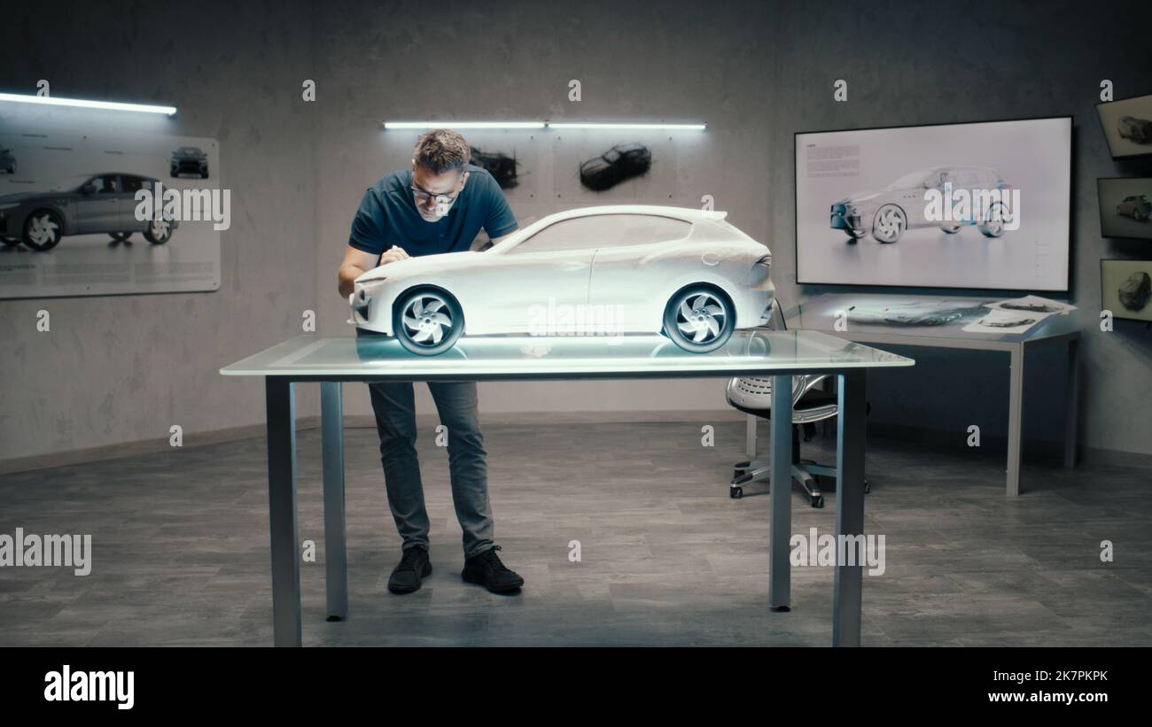 Ein Automobilingenieur und -Designer arbeitet in einem modernen Studio mit heller LED eines Automobilkonzerns an einem Prototyp-Modellauto. Konstruktionskorrekturen Vornehmen. Stockfoto