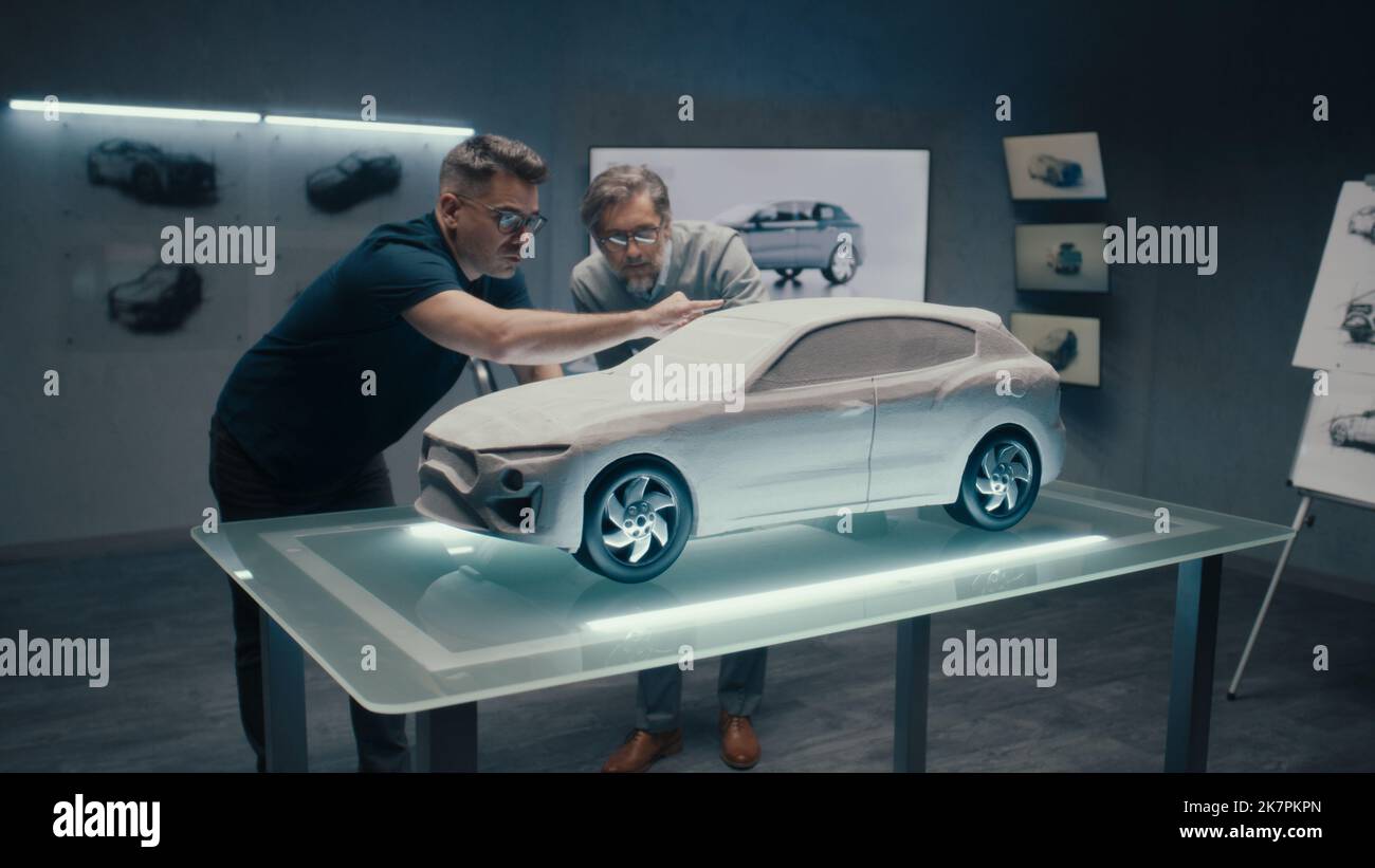 Erfahrene Automobildesigner und Autoentwickler diskutieren das Design vor einem auf einem Glastisch platzierten Rechen-Modell. Ein High-Tech-Laborraum mit LED und Skizzen. Stockfoto