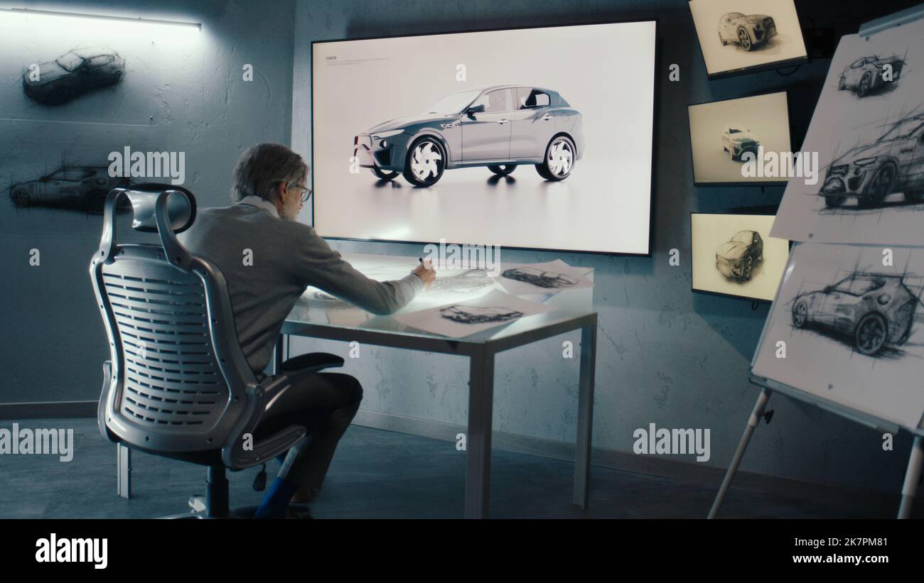 Senior Automotive Grafikdesigner arbeitet mit digitalen Display-Grafiken Touch sreen Tisch. Betrachtet das rotierende 3D-Bild des Fahrzeugs in einer an der Wand montierten LED. Innovatives Hightech-Labor. Stockfoto