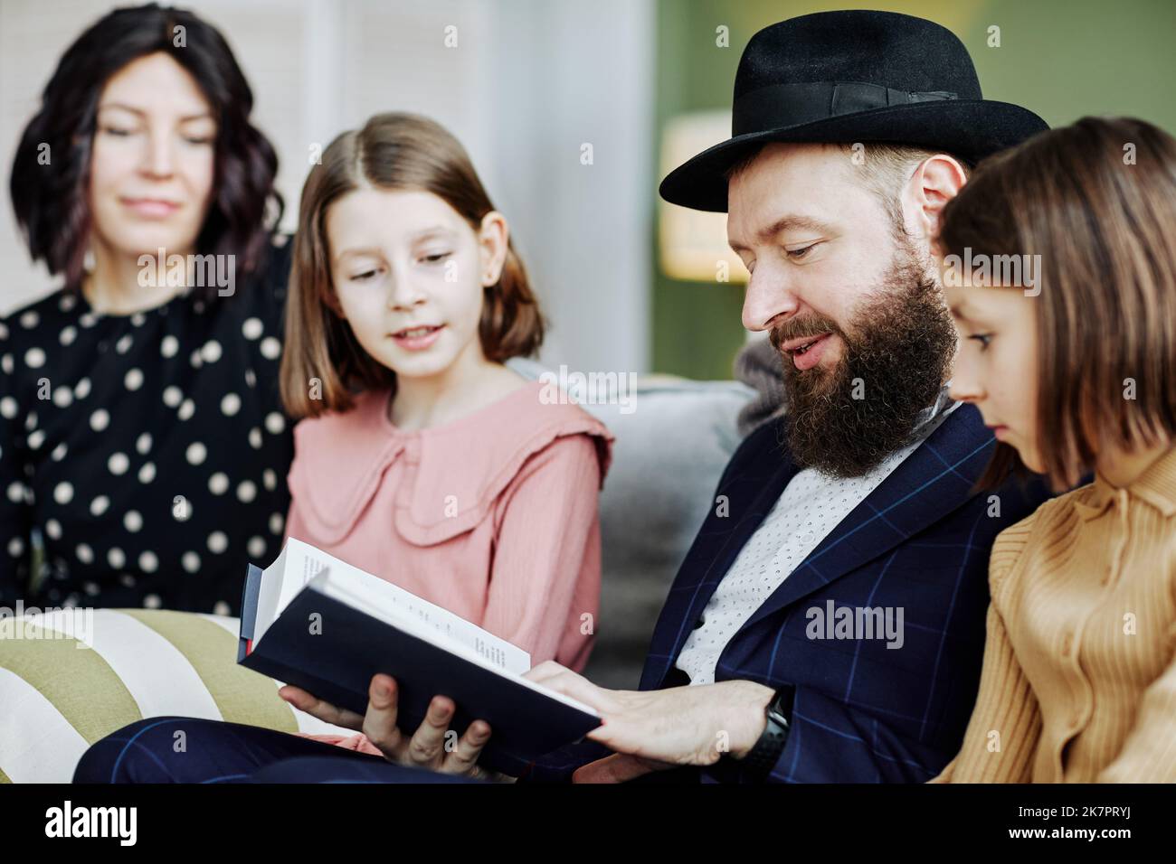 Seitenansicht Porträt eines orthodoxen jüdischen Mannes, der im häuslichen Umfeld ein Buch für Kinder liest Stockfoto