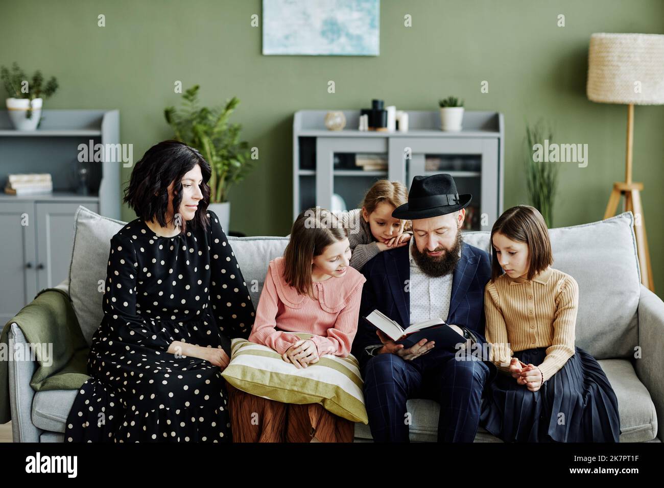 Porträt einer jüdischen Familie mit drei Kindern, die gemeinsam Buch lesen, in einem modernen Zuhause Stockfoto