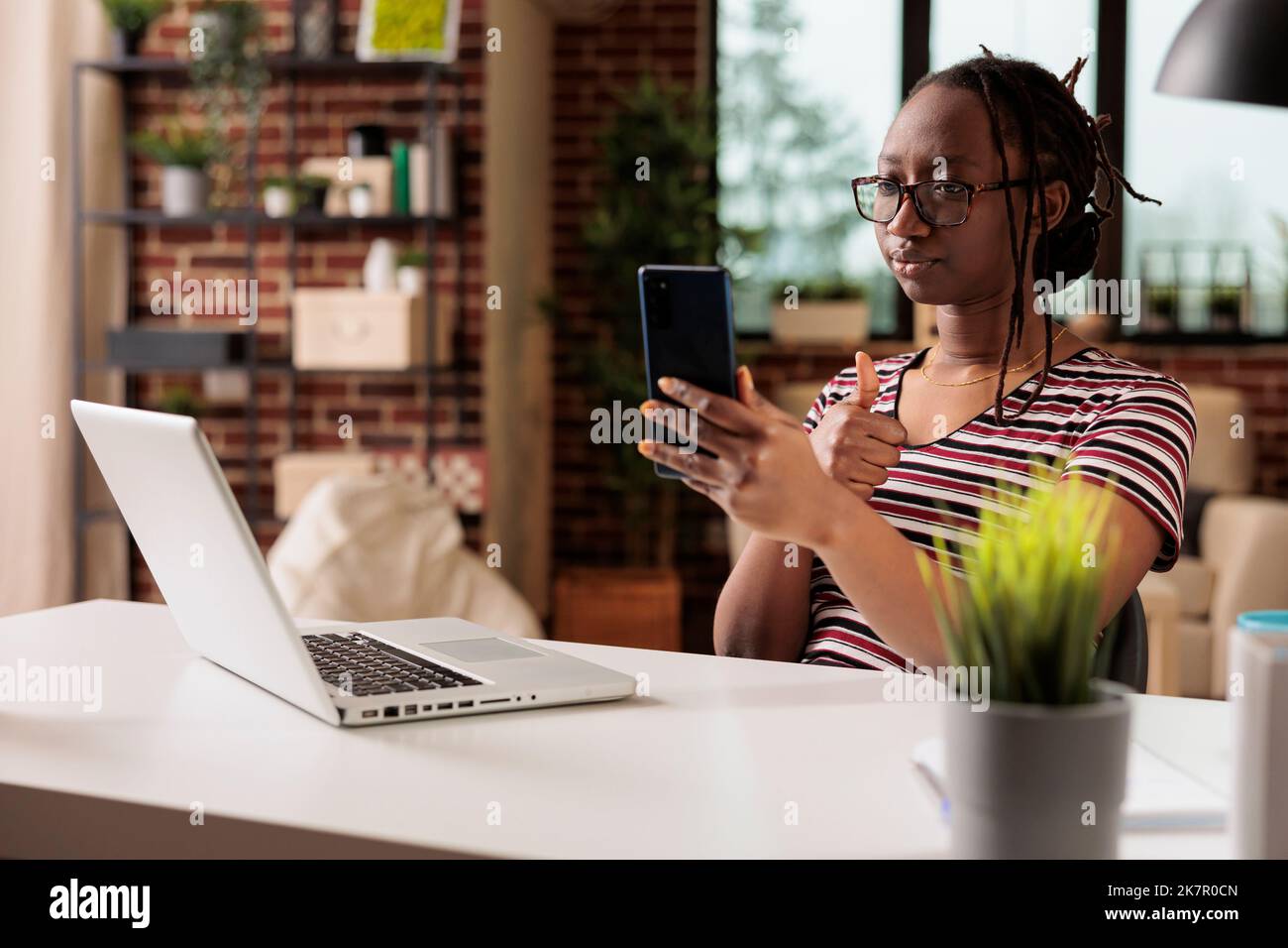 Freiberuflerin zeigt Wertschätzung Geste auf Smartphone-Videocall, Frau arbeitet von zu Hause aus. Mitarbeiter mit Daumen nach oben, der an einem virtuellen Meeting teilnimmt, Remote-Mitarbeiter chattet bei Telefonkonferenzen Stockfoto
