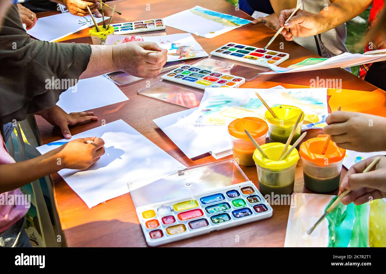 Mehrere Menschen zeichnen auf Papier mit Aquarellfarben, die am gleichen Tisch sitzen. Masterclass „Zeichnen“. Hände und Tisch aus der Nähe, ohne Gesicht Stockfoto