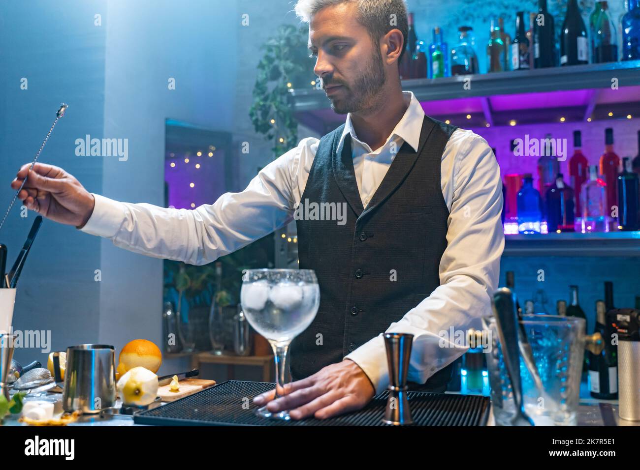 Barkeeper in einem weißen Hemd und schwarzer Schürze, der bei einer Party im Nachtclub Cocktails zubereitet. Nachtleben. Stockfoto