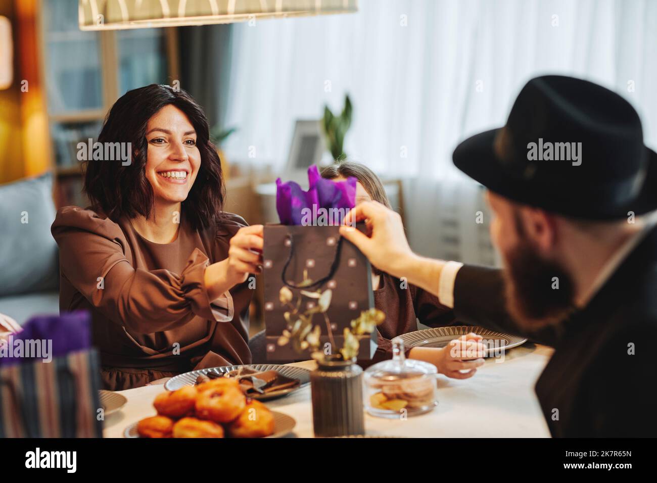 Porträt eines erwachsenen jüdischen Paares, das Geschenke am Esstisch in gemütlicher Wohnumgebung teilt Stockfoto